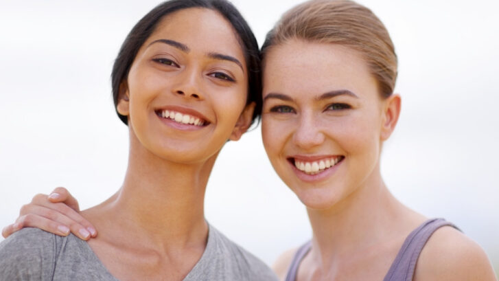 Two women smiling together, demonstrating healthy teeth and gums for oral health education.