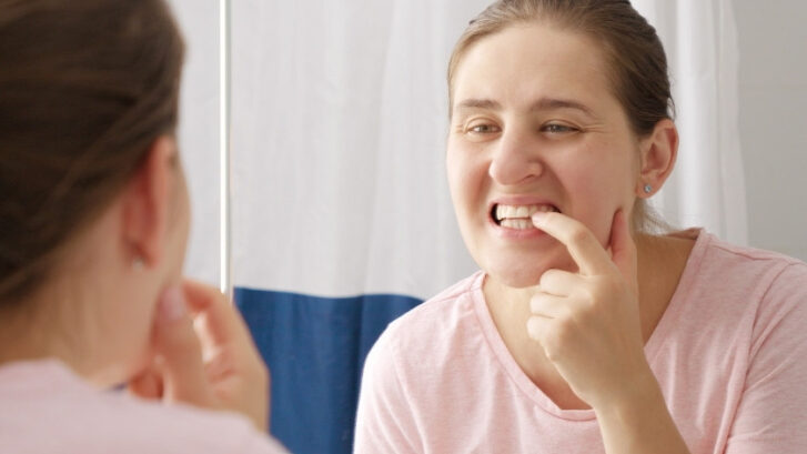 Woman examining her teeth in mirror, checking for signs of dental problems.