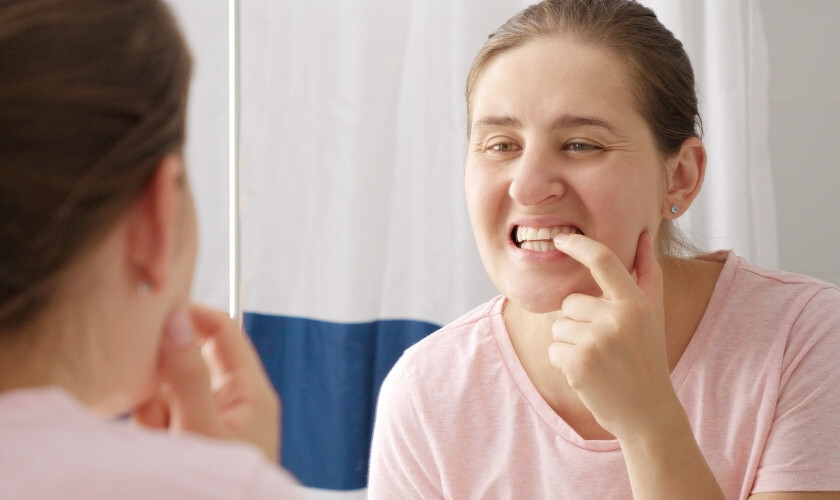 Woman examining her teeth in mirror, checking for signs of dental problems.