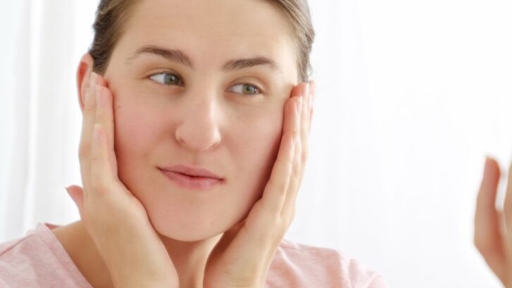 Woman with dry lips touching her face, concerned about lip dryness and dental health.