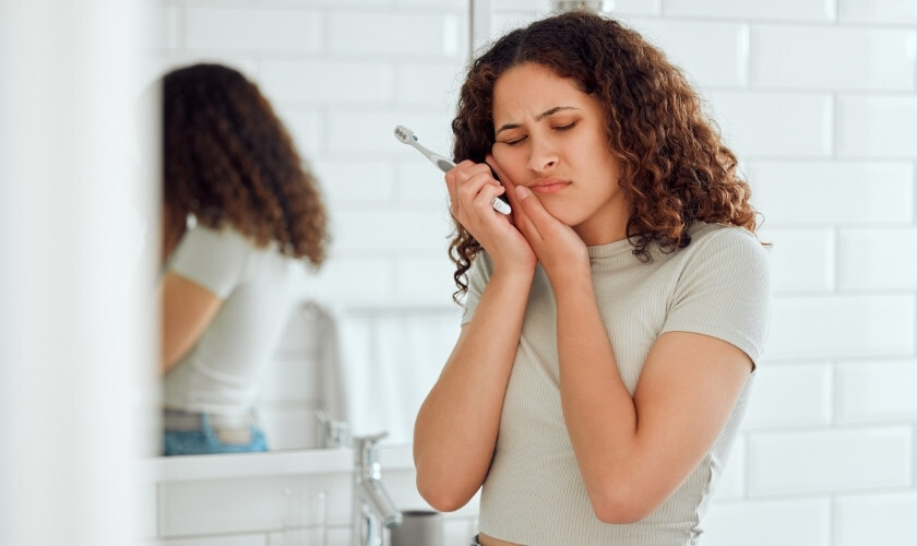 Woman applying toothpaste with brush while looking in bathroom mirror.