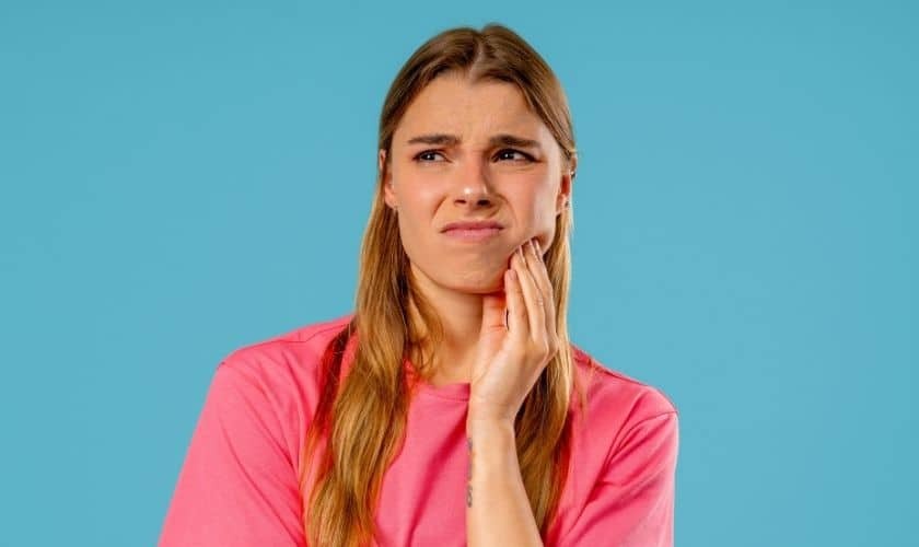 Woman in pink shirt touching her cheek in pain, depicting dental discomfort or tooth sensitivity.