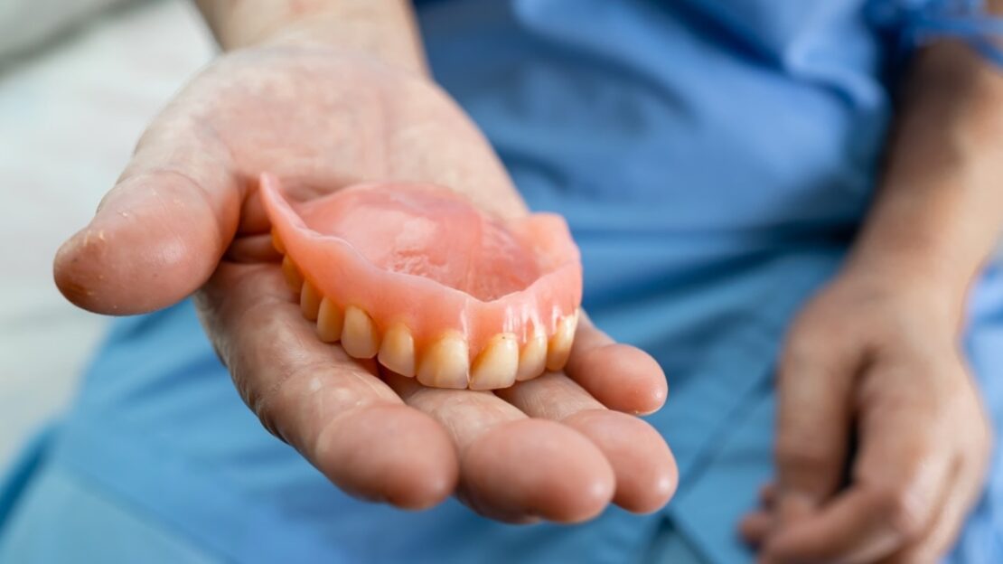 Dentist holding a complete upper denture showing natural-looking teeth in Snellville, GA.