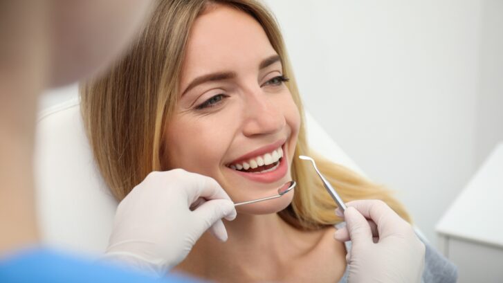 Smiling patient receiving dental examination with professional instruments during cosmetic dentistry consultation.