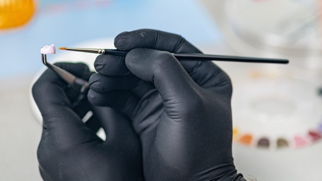Dentist in black gloves holding fine detail brush for precision dental work.