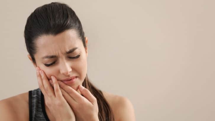 Woman holding her cheek with a pained expression, experiencing dental discomfort.