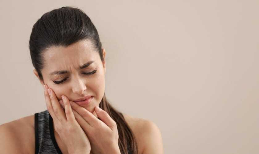 Woman holding her cheek with a pained expression, experiencing dental discomfort.