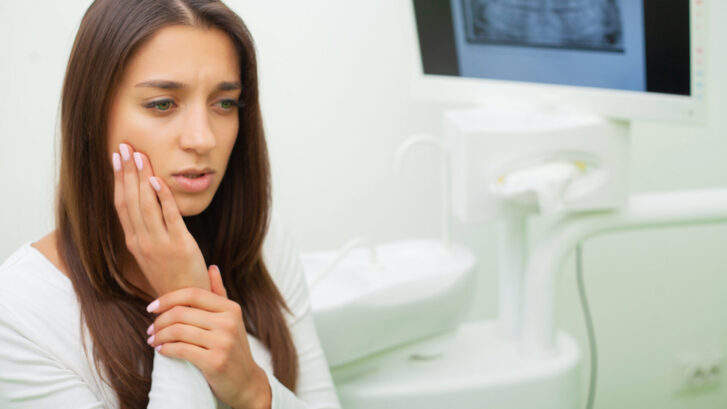 Woman holding her cheek in a dental office, experiencing tooth pain.
