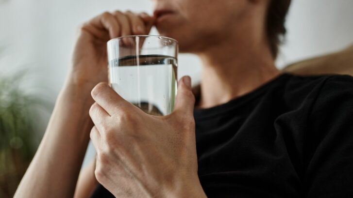 Person drinking a glass of water to help relieve dry mouth symptoms.