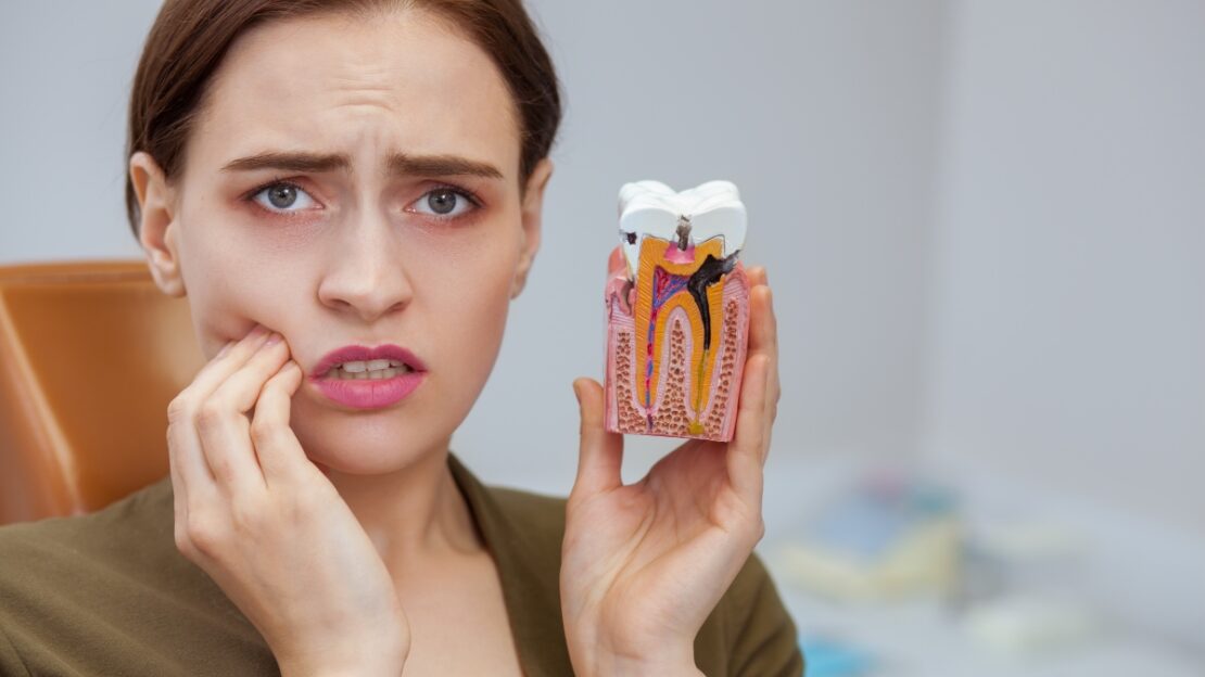 Woman with concerned expression holding a dental cross-section model showing tooth decay and infection.