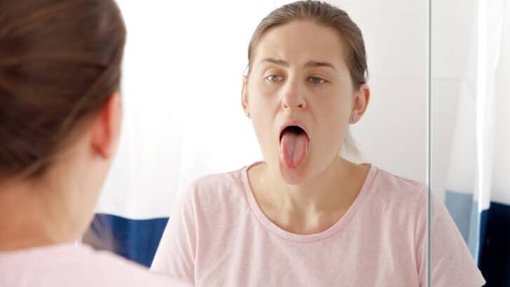 Woman examining her tongue in mirror to check for bumps or oral lesions.