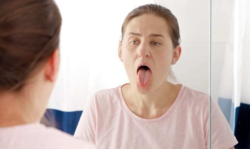 Woman examining her tongue in mirror to check for bumps or oral lesions.