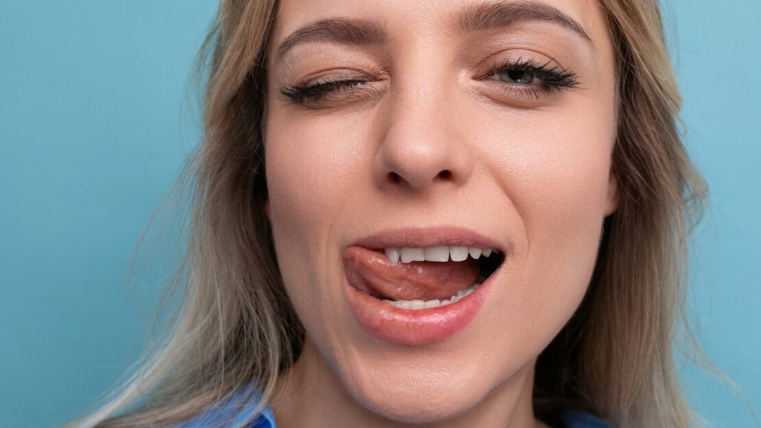 Woman with open mouth showing tongue and teeth against blue background.