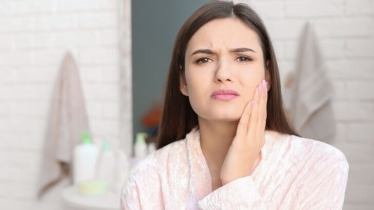Woman holding her cheek in discomfort, illustrating dental pain from a chipped tooth.