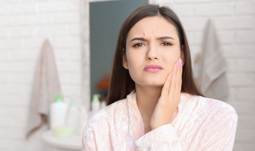 Woman holding her cheek in discomfort, illustrating dental pain from a chipped tooth.