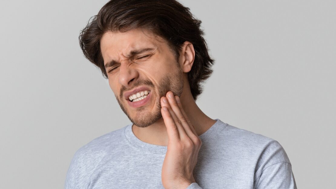Man experiencing tooth pain, holding his cheek in discomfort.
