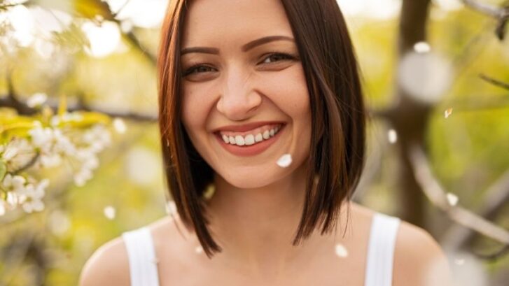 Woman smiling outdoors among blooming flowers, demonstrating a healthy, bright smile.