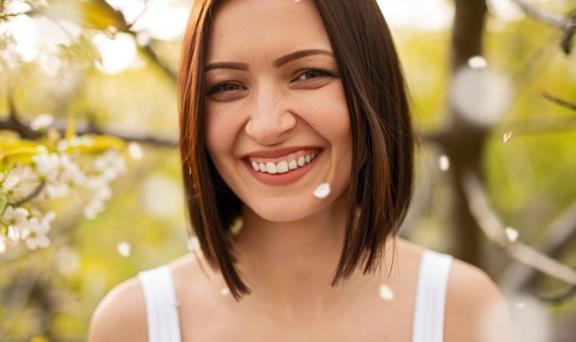 Woman smiling outdoors among blooming flowers, demonstrating a healthy, bright smile.