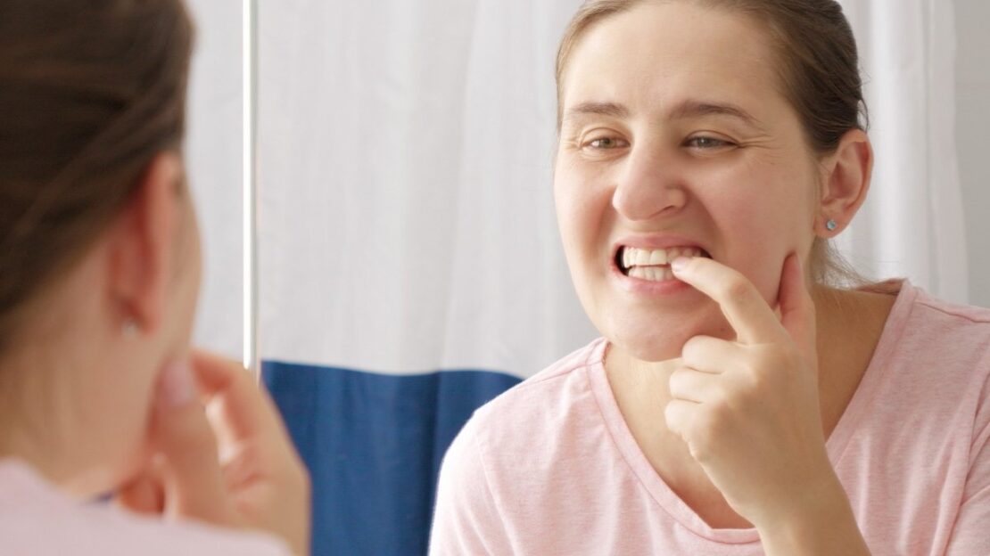 Woman examining her teeth in mirror while flossing for gum health.