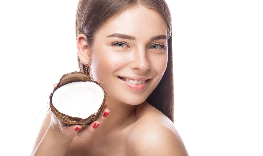 Smiling woman holding a halved coconut while discussing oil pulling benefits for dental health.