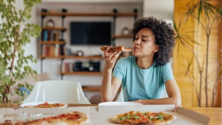 Woman enjoying pizza at home, considering dietary adjustments after dental implant placement.