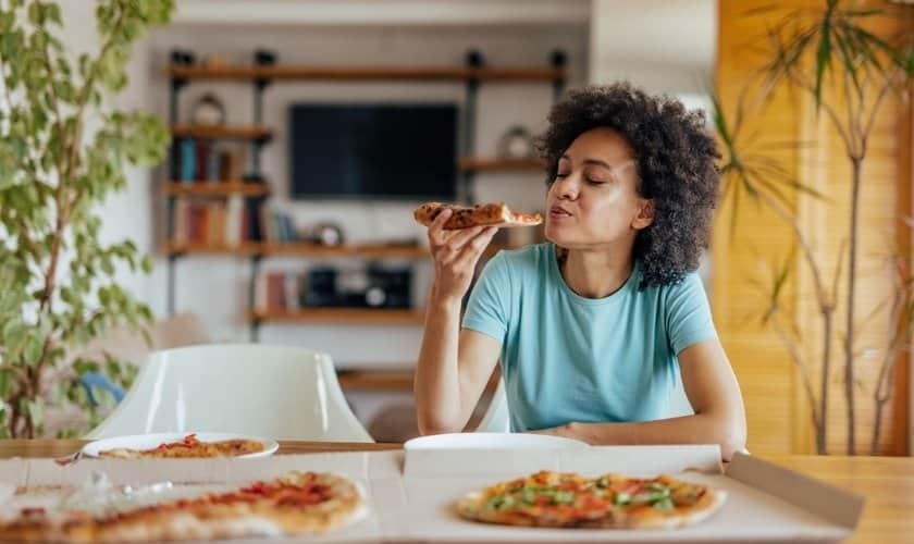 Woman enjoying pizza at home, considering dietary adjustments after dental implant placement.