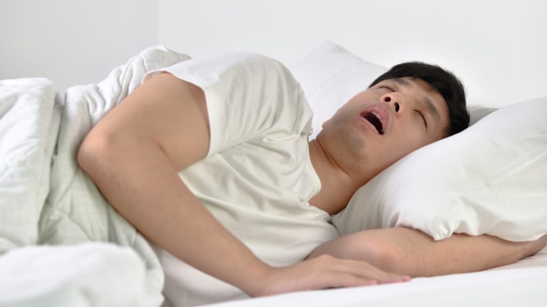 Man sleeping peacefully in bed, illustrating the restorative rest improved by sleep apnea treatment.