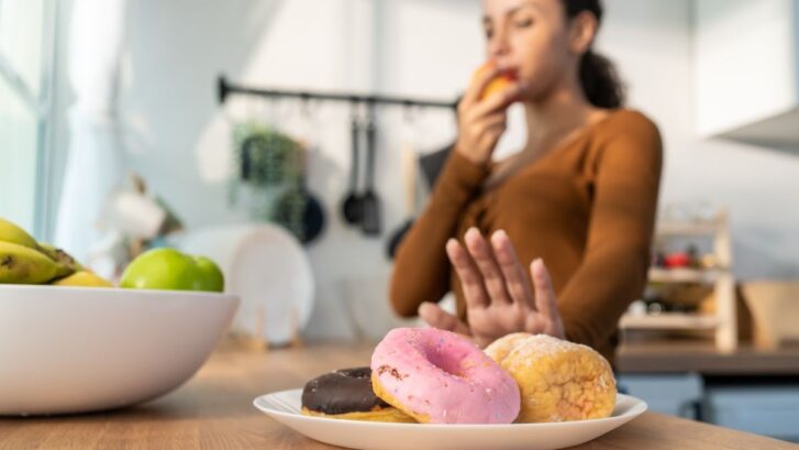 Woman refusing donuts while eating an apple during recovery after tooth extraction.