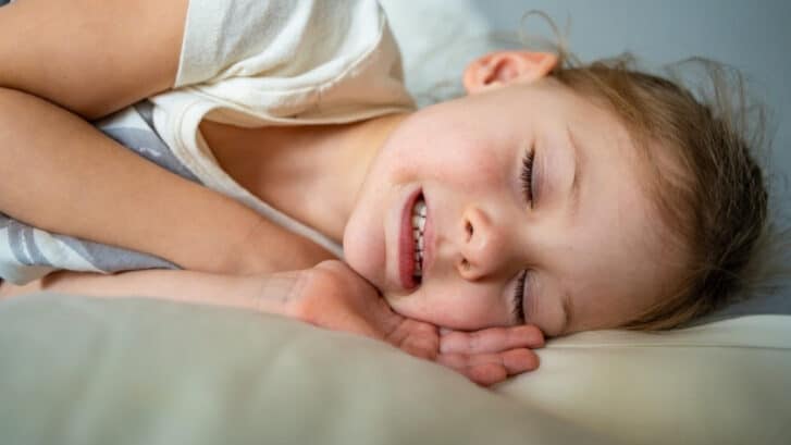 Young child sleeping peacefully with mouth open, illustrating nighttime teeth grinding concerns.