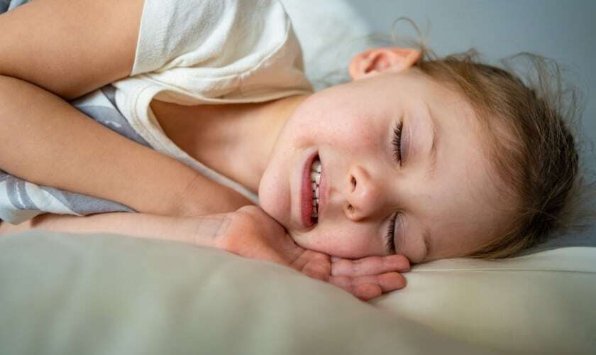 Young child sleeping peacefully with mouth open, illustrating nighttime teeth grinding concerns.
