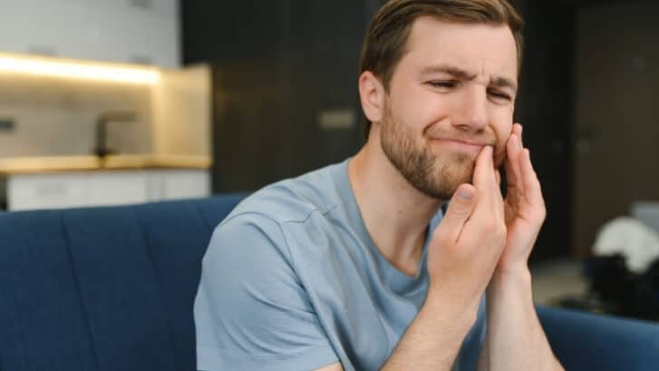 Man holding cheek experiencing tooth pain while considering treatment options.