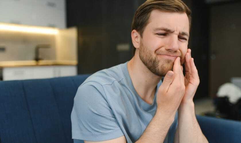 Man holding cheek experiencing tooth pain while considering treatment options.
