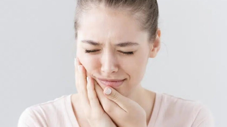 Woman experiencing jaw pain, holding her face in discomfort after root canal treatment.
