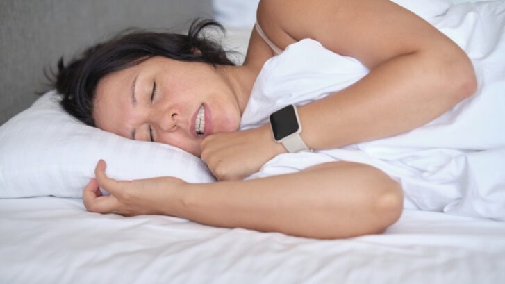 Woman sleeping peacefully while wearing smartwatch, illustrating stress relief from TMJ therapy.