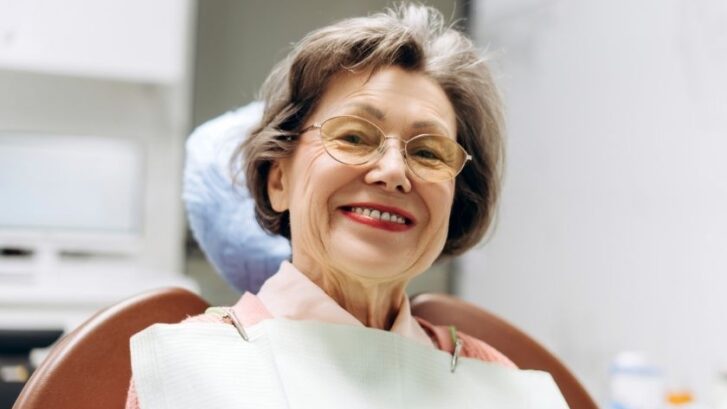 Smiling mature woman with glasses in a dental office setting.