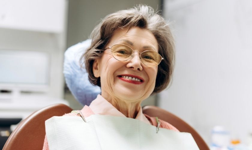 Smiling mature woman with glasses in a dental office setting.