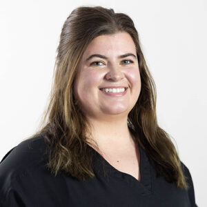 Woman smiling at camera wearing black scrubs, professional headshot for dental practice.