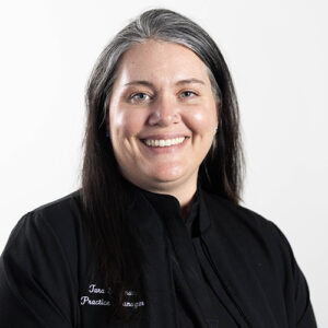 Professional headshot of smiling woman in black dental scrubs against white background.