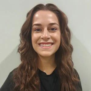 Young woman smiling at camera in professional headshot against neutral background for dental practice.